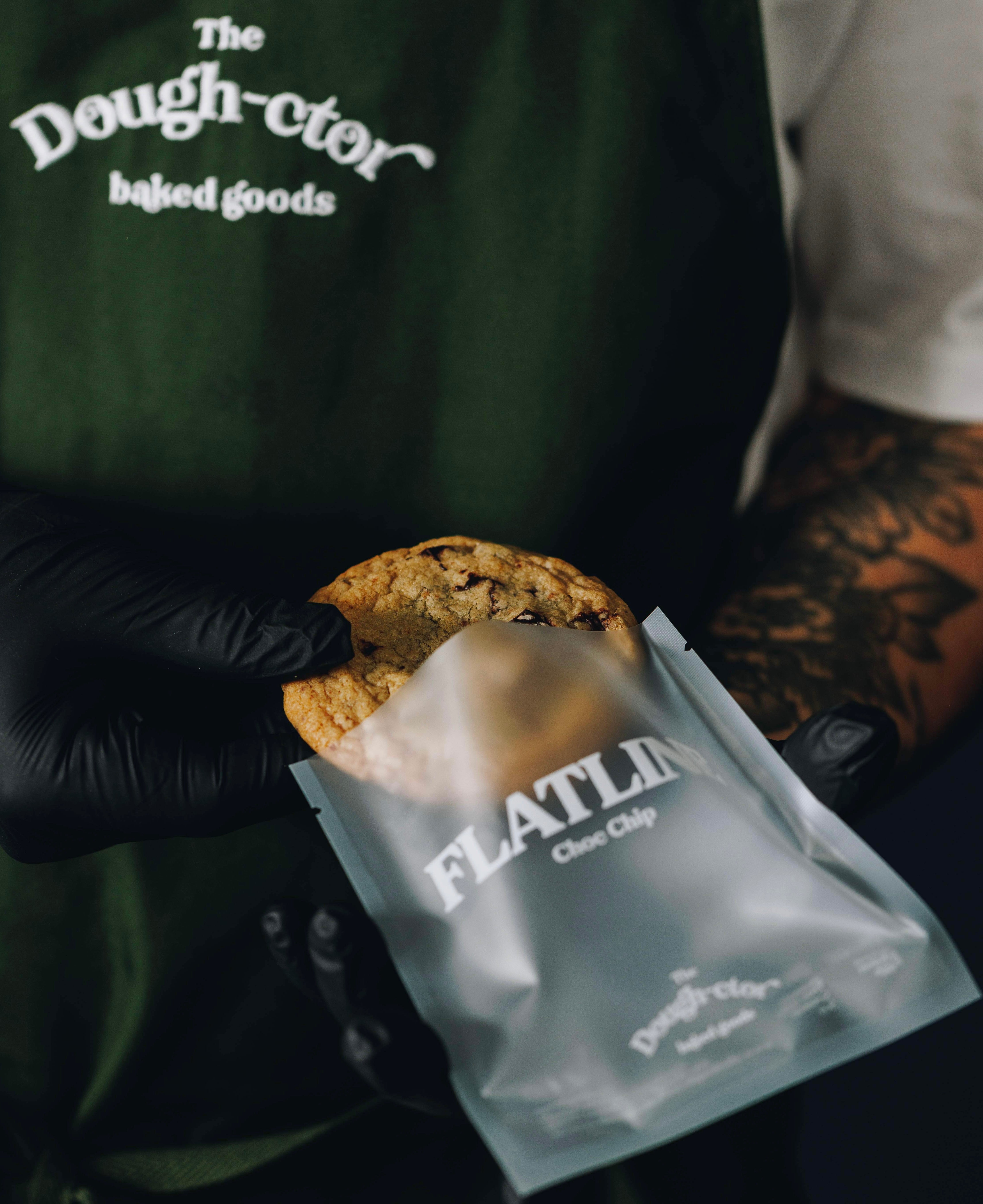 Flatline cookies - Flatline cookies placed in packaging - dark green apron - The Dough-ctor Baked Goods
