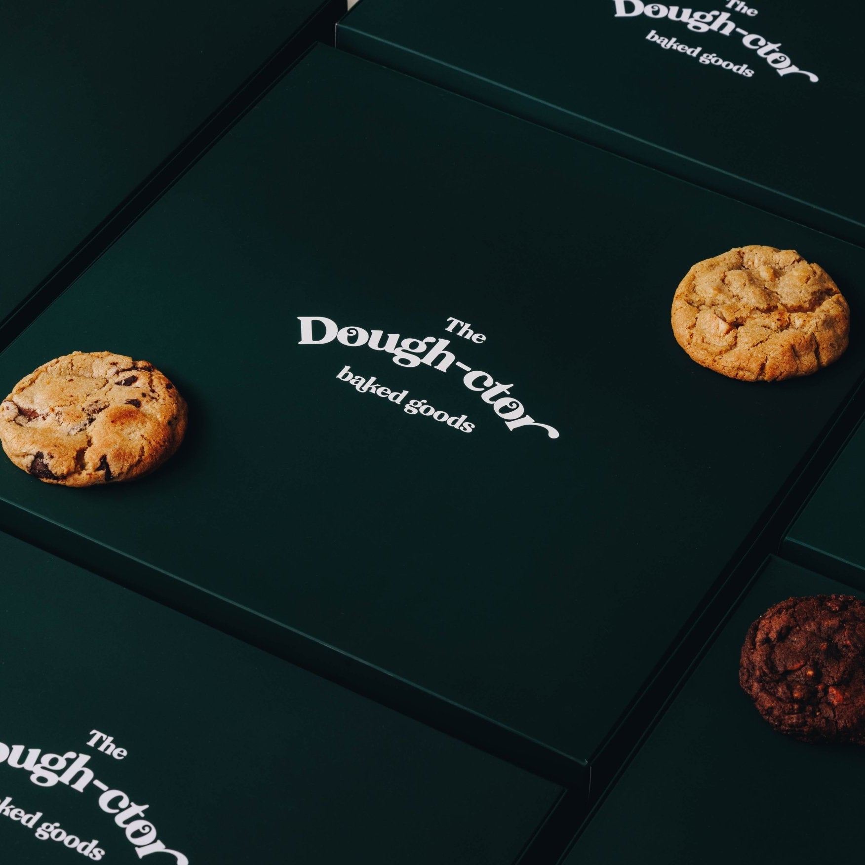 Dark green box - 12 pack Variety - flatline 12 pack - The Dough-ctor Baked Goods - closed box - cookies on box - angled view