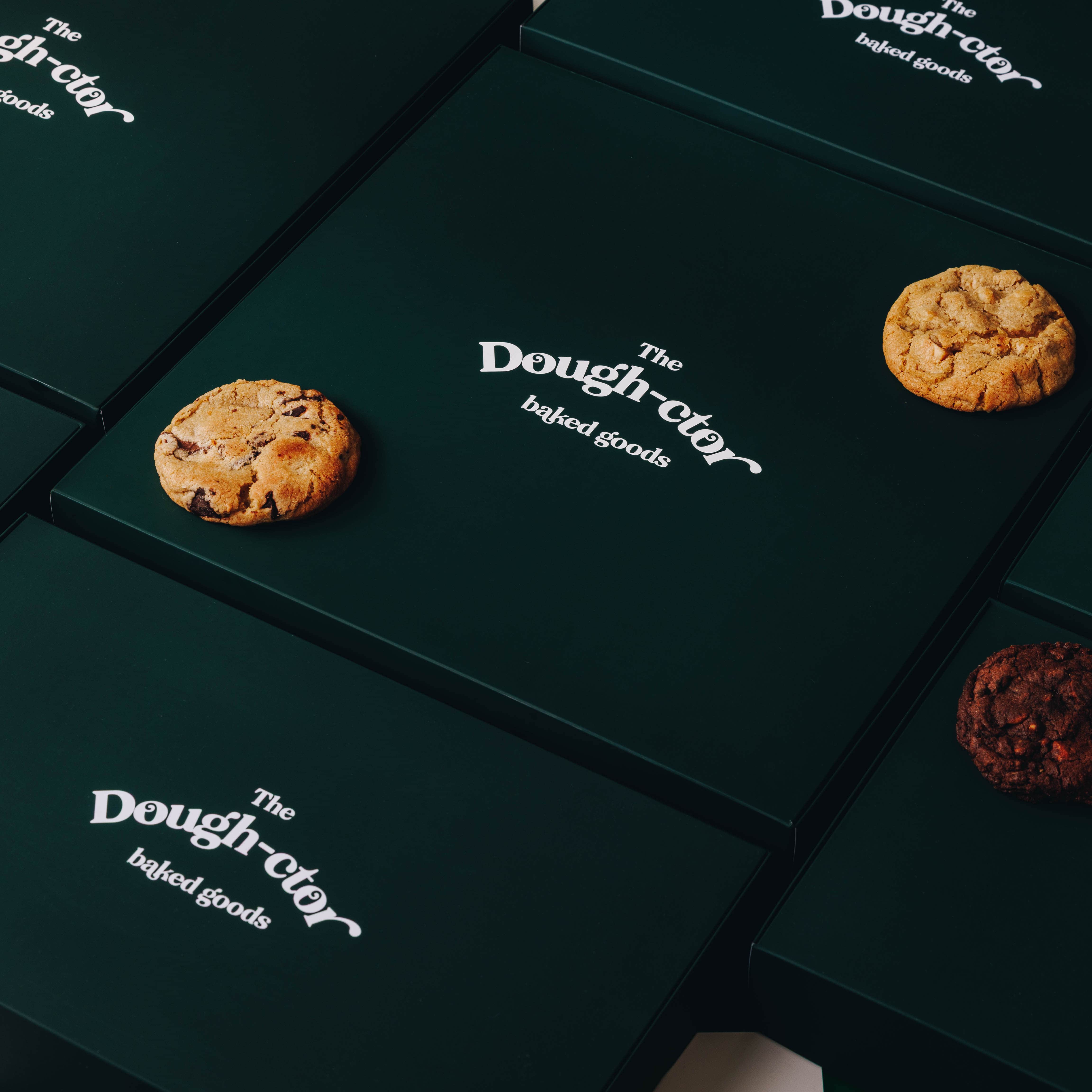 Dark green boxes with 'The Dough-ctor' branding and cookies on top.