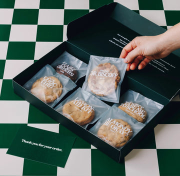 Variety Pack - The Dough - ctor Baked Goods - 6 - pack variety - opened box - hand reaching grabbing a cookie - angled View